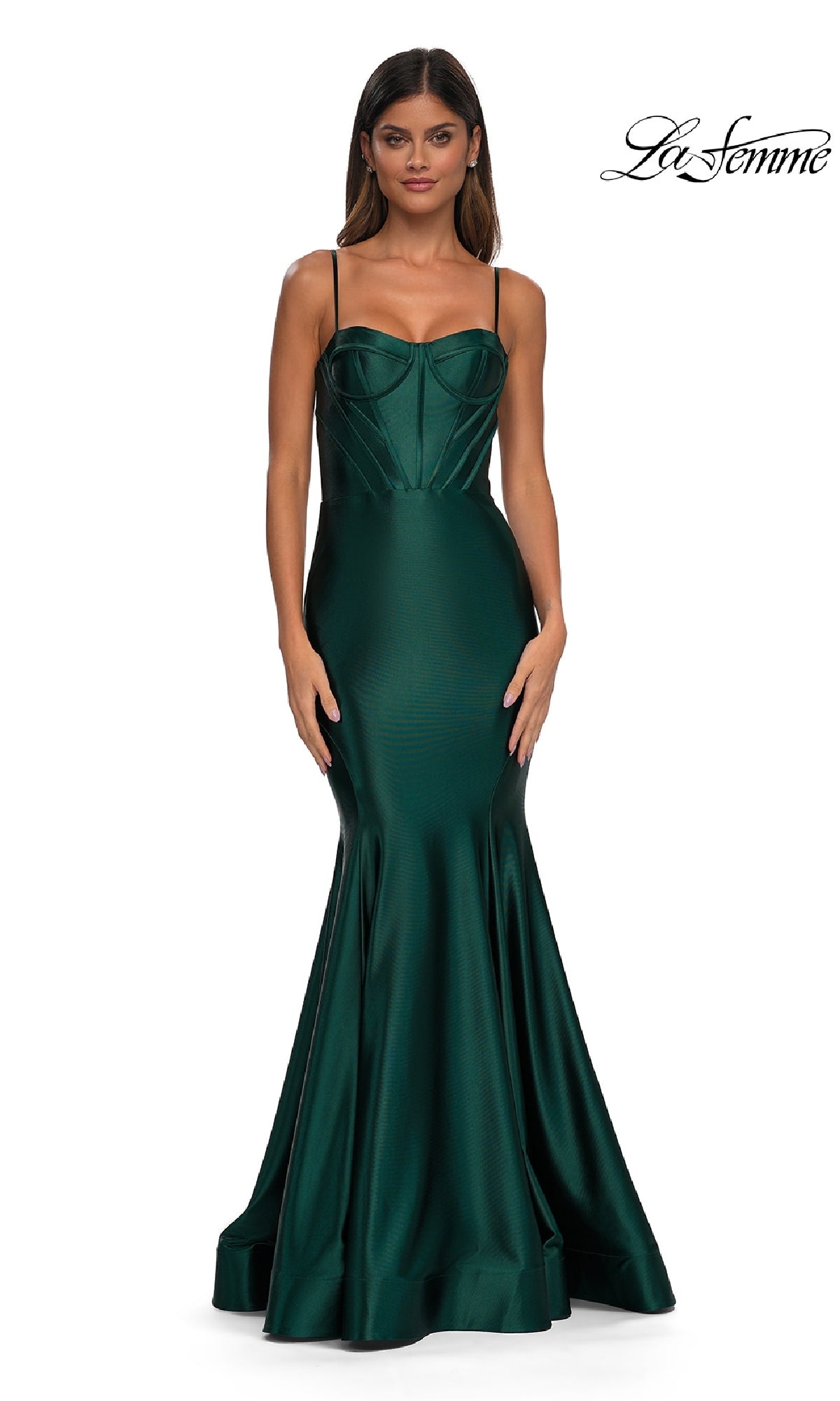 A woman models the La Femme 32555 Long Corset Mermaid Prom Dress in fitted emerald green satin with thin straps, standing against a plain white background. The La Femme logo appears in the top right corner.